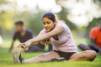 Adolescente assise dans l'herbe avec une jambe tendue tout en se penchant en avant pour toucher ses orteils avec les deux mains