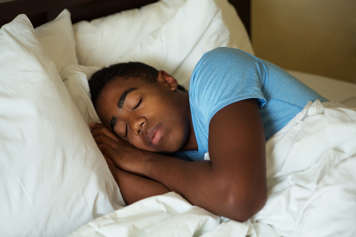 Adolescent dormant sur son côté dans son lit, les mains près de son visage sur son oreiller