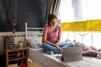 Teen girl sitting on her bed having a therapy session with her therapist via video call