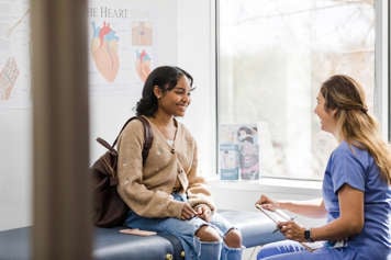 Teen girl sitting on an exam table talking to a health-care provider