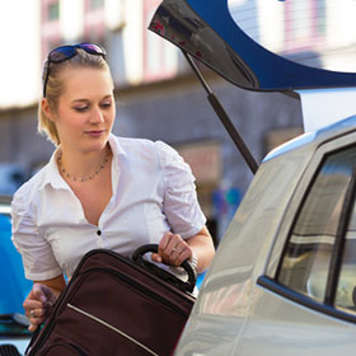 Teen girl putting suitcase in trunk of car